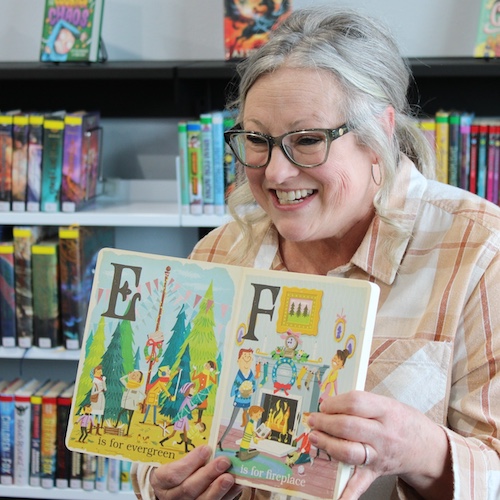 A woman holds a picture book open, smiling